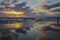 Panoramic scene of ocean sunset with clouds reflected on wet beach and person wading