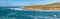 Panoramic seascape in blue and turquoise colors. Pacific ocean, rocky cliffs, and silhouette of Morro Rock.