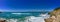 Panoramic shot of beautiful sea waves surrounded by cliffs under the blue sky