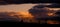 Panoramic shot of the cloudy sky during the sunset above the silhouette of the land