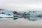 Panoramic shot of Fjallsarlon glacier lagoon at the end of Vatnajokull glacier. Icebergs reflects in the calm water. Foggy weather