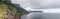 Panoramic shot of green karst cliffs of Cabo Antzoriz and grey, rippling waters of Bay of Biscay on cloudy, rainy summer morning.