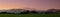 Panoramic shot of a greenfield on a mountain landscape background during sunt