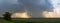 Panoramic shot of large stormy clouds over a meadow