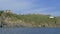 Panoramic shot of rocky shore overgrown with green vegetation with small village and lighthouse located on shore