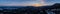 a panoramic shot of the sun setting behind a mountain ridge that contains some trees