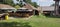 Panoramic shot of two wooden barns next to a house on a grass field on a sunny day