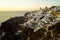 Panoramic skyline scene in sunset light of Oia village and white building townscape along island natural mountain facing ocean