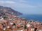 Panoramic sunlit view of the city of funchal from above with rooftops and buildings in front of a bright blue sea