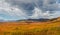 Panoramic sunny motley autumn landscape with sunlit gold big valley under cloudy sky. Awesome alpine scenery with beautiful high