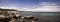 Panoramic tranquil seascape of a rocky beach in a small Cape Cod village. Many beach rocks and idyllically floating white clouds o