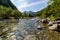 Panoramic valley landscape with crystal clear river, stones, and tall trees in Ordesa Pirineos. Reflections in the water and