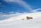 Panoramic view across snow covered slope on alpine mountain with small house