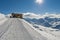 Panoramic view across snow covered slope on alpine mountain with small hut