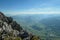 A panoramic view from an Alpine top on a vast valley. There are sharp mountains and high peaks around. Alpine slopes