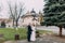 Panoramic view of beaytiful newlywed couple holding hands in park near old baroque church