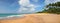 Panoramic view of deserted beach with footprints and lush palm trees