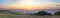 Panoramic view from Ditchling Beacon during sunset, with a dramatic cloudy sky and grass meadows in the foreground.