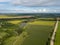 Panoramic view from drone to the countryside with a river, dirt road and agricultural fields against cloudy sky