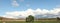 Panoramic view of large open dry drought affected farm fields under stretching cloud filled blue skies and a lone tree in rural