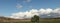 Panoramic view of large open dry drought affected farm fields under stretching cloud filled blue skies and a lone tree in rural