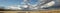 Panoramic view of large open dry drought affected farm fields under stretching cloud filled blue skies over properties in rural