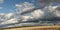 Panoramic view of large open dry drought affected farm fields under stretching cloud filled blue skies over properties in rural