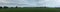 Panoramic view of large open farm fields and stretching rain filled cloudy overcast skies over lush green sheep pasture paddocks,