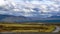 Panoramic view of mountaineous landscape with winding road and cyclist beneath dramatic sky