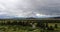 Panoramic View of Mountains under dark clouds on the horizon and upscale log cabin and pond and bridge in foreground -selective fo