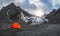 Panoramic view of an orange fortified tent on the background of a glacier on a high-altitude plateau. Extreme overnight stay in