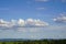 Panoramic view over fields orchards meadows towards mountains on the horizon. Above, huge white clouds shine from the blue spring