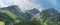 Panoramic view of row of mountains and forest with a blue sky and couds.