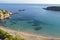 Panoramic view of sandy beach, boat, mountains, cliffs, sea and blue sky.