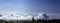 Panoramic view of Scandinavian mountain range covered by ice and snow, blue skies, pine forest below the tops