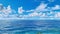 Panoramic view of a serene ocean, under a clear blue sky adorned with fluffy clouds