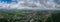 Panoramic view of a small town with spacious, green surfaces under a cloudy sky