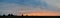 Panoramic view of the sunset sky and clouds in the field and the silhouette of several trees on the horizon