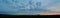 Panoramic view of the sunset sky and clouds in the field and the silhouette of several trees on the horizon