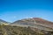 : Panoramic view of volcano Etna against an intense blue sky. Horizontal view of the central crater. A row of people trying to