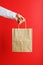 Paper bag at arm`s length, brown craft bag for takeaway isolated on red background. Packaging template layout with space for