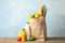 Paper bag with groceries on wooden table against blue background