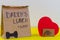 Paper bag and red heart on yellow wooden desk.