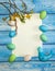 Paper blank,  branches with buds and flowers, a handmade textile bird and Easter eggs on a light blue wooden background.