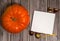 Paper blank, pen, orange pumpkin, chestnut fruit in an open shell on a wooden background.