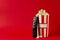 Paper box full of sweet pop corn and tv clicker on the bright red background.Empty space