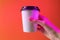 Paper coffee cup in a hand in a trendy neon light.