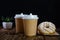 Paper cups of coffee, sugar in bags, donuts. Wooden table. Black background