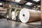 Paper mill with workers operating machinery to produce paper rolls, large vats filled with pulp, recycling and sustainability