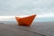 Paper orange boat on a railing with sky and ocean background